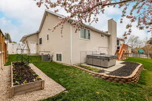 Back of house featuring a fenced backyard, stucco siding, a hot tub, a chimney, and a garden