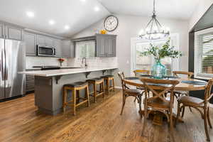 Kitchen with gray cabinets, stainless steel appliances, dark wood-style flooring, a peninsula, and a kitchen breakfast bar