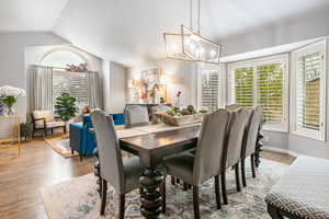 Dining space with vaulted ceiling, wood finished floors, plenty of natural light, and a chandelier