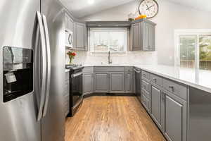 Kitchen with gray cabinets, stainless steel appliances, light wood-type flooring, vaulted ceiling, and tasteful backsplash
