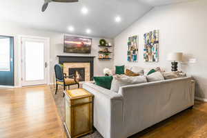 Living room featuring a stone fireplace, wood finished floors, lofted ceiling, ceiling fan, and recessed lighting