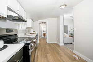 Kitchen with electric range, light wood-type flooring, white cabinets, and light stone countertops
