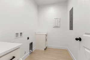 Laundry area with hookup for a washing machine, cabinet space, hookup for an electric dryer, light wood-style flooring, and electric panel