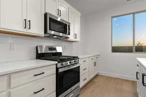 Kitchen featuring stainless steel appliances, white cabinets, light wood-style floors, backsplash, and light stone countertops