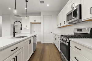 Kitchen featuring stainless steel appliances, white cabinets, dark wood-style floors, pendant lighting, and light stone countertops