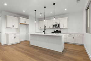 Kitchen with backsplash, an island with sink, white cabinets, and decorative light fixtures