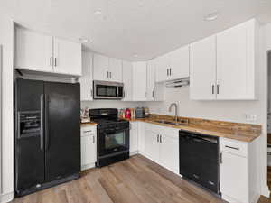 Kitchen with black appliances, white cabinetry, light stone countertops, light wood-style floors, and a textured ceiling