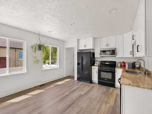 Kitchen featuring black appliances, light stone countertops, white cabinets, light wood-style floors, and a textured ceiling
