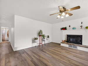 Unfurnished living room featuring ceiling fan, dark wood-type flooring, a textured ceiling, and a glass covered fireplace