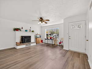 Foyer entrance with wood finished floors, ceiling fan, a textured ceiling, and a glass covered fireplace