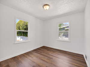 Spare room featuring dark wood-type flooring, a textured ceiling, and plenty of natural light