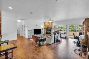 Tiled living room featuring an office area, a stone fireplace, a textured ceiling, and a ceiling fan