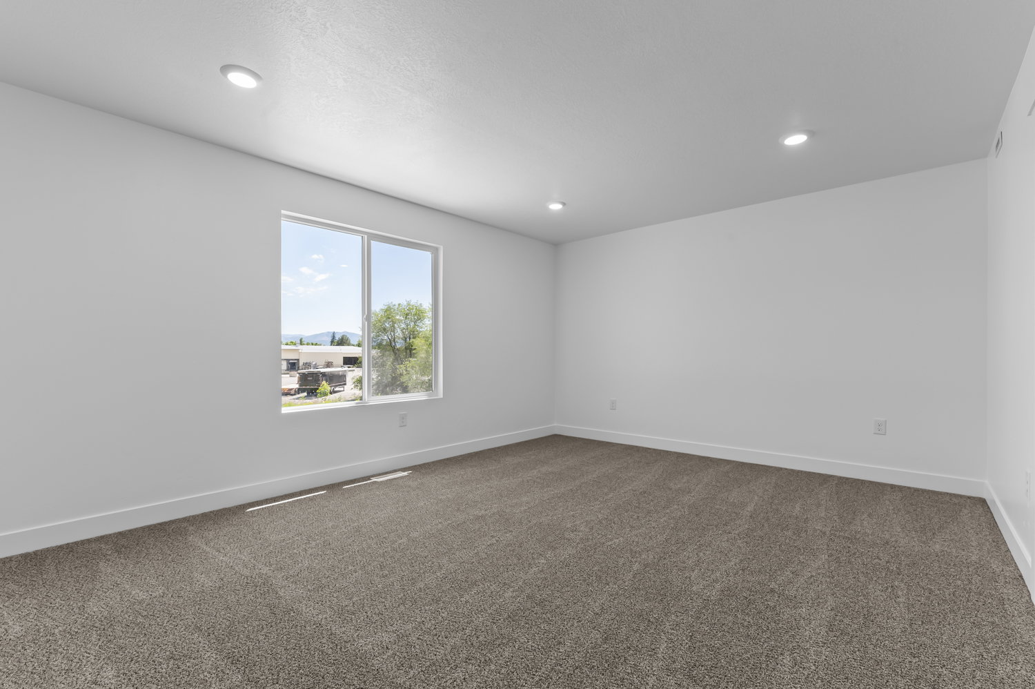 Spacious room featuring neutral carpeting, white walls, recessed ceiling lighting, and a large window