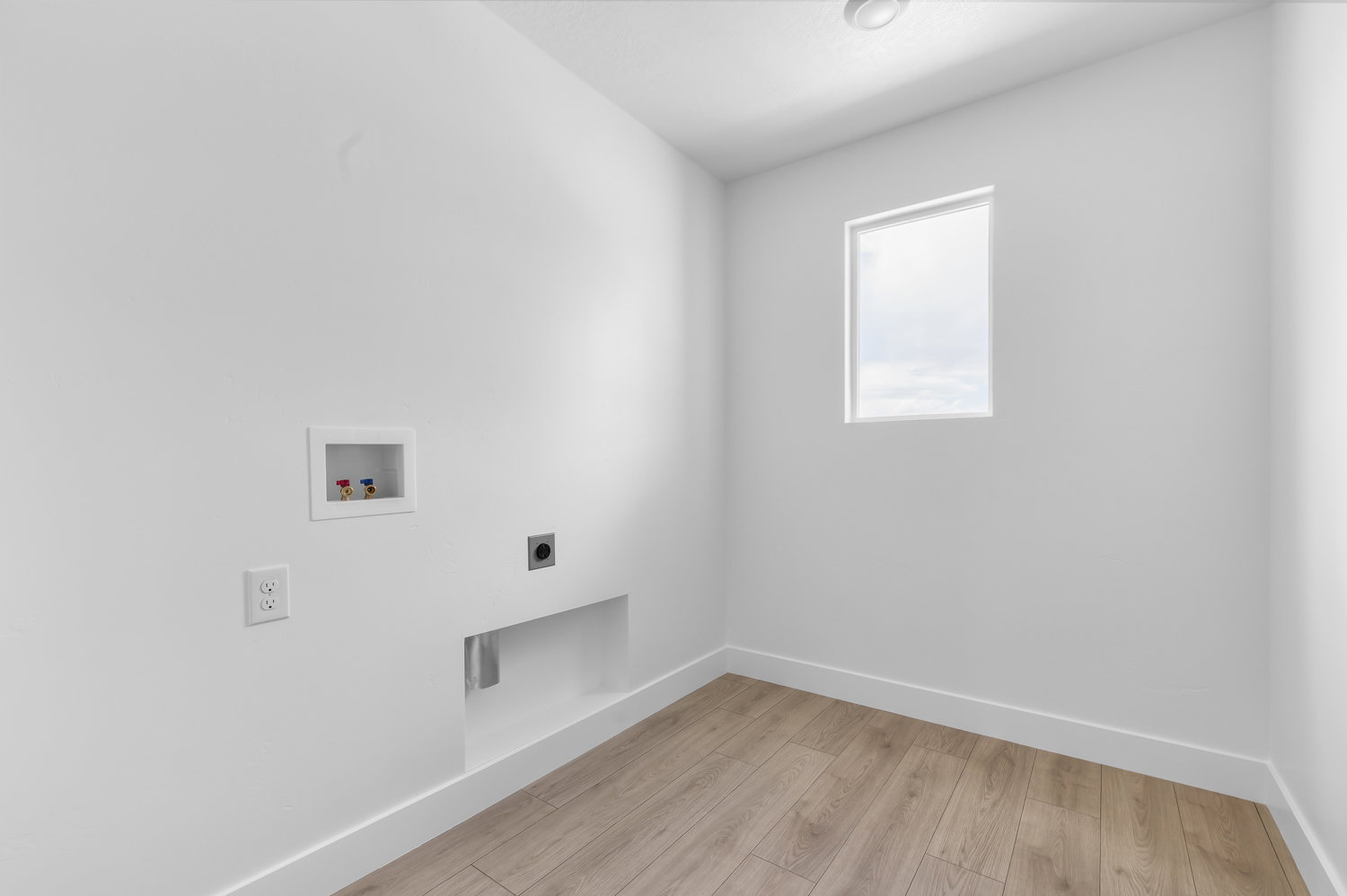 Utility room featuring wood-finish flooring, white baseboards, a single window, and visible plumbing connections for a washing machine