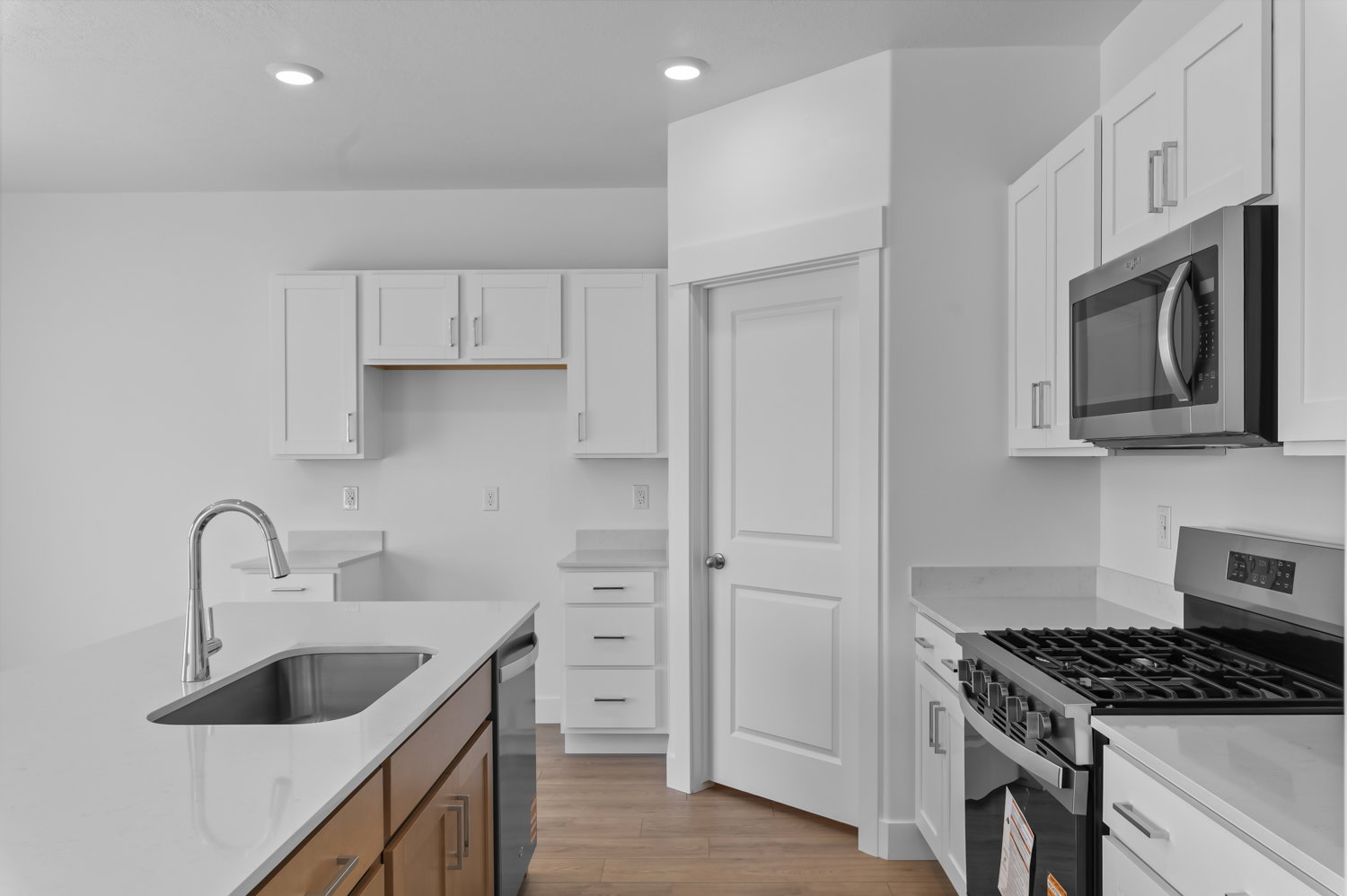 Modern kitchen featuring white shaker cabinetry, stainless steel appliances, light-toned countertops, a kitchen island with a stainless steel sink, and wood-finish flooring