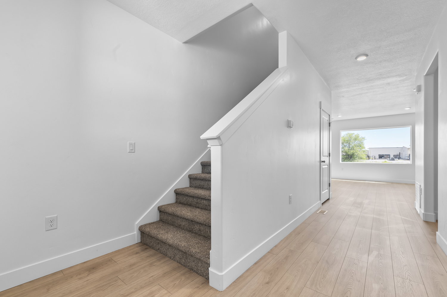 Carpeted staircase with white balustrade, light wood-finish flooring, white baseboards, and a large picture window