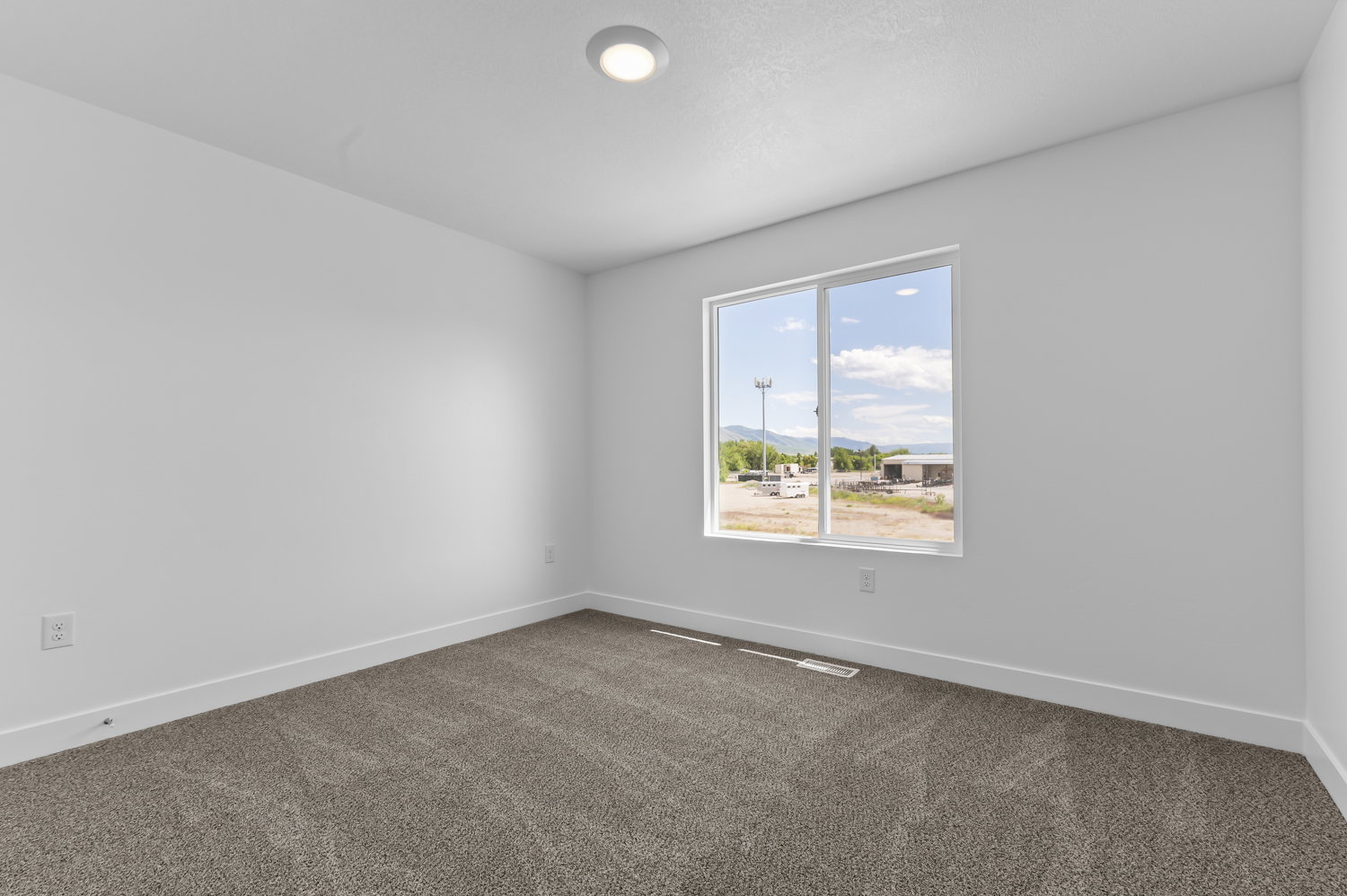 Spacious room featuring neutral carpeting, white baseboards, and a large window with a distant mountain backdrop