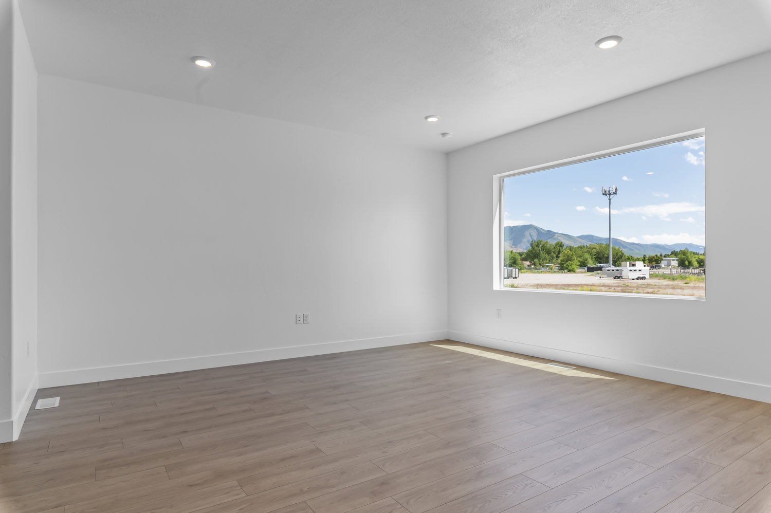 Spacious room featuring a large horizontal window, light wood-finish flooring, white painted walls, white baseboards, and recessed ceiling lighting