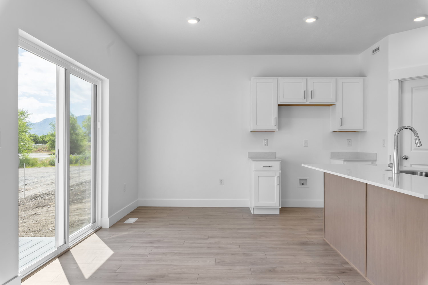 Open-concept kitchen and dining area featuring wood-finish flooring, white shaker-style cabinetry with minimalist hardware, and a center island with a white countertop and light wood-tone paneling