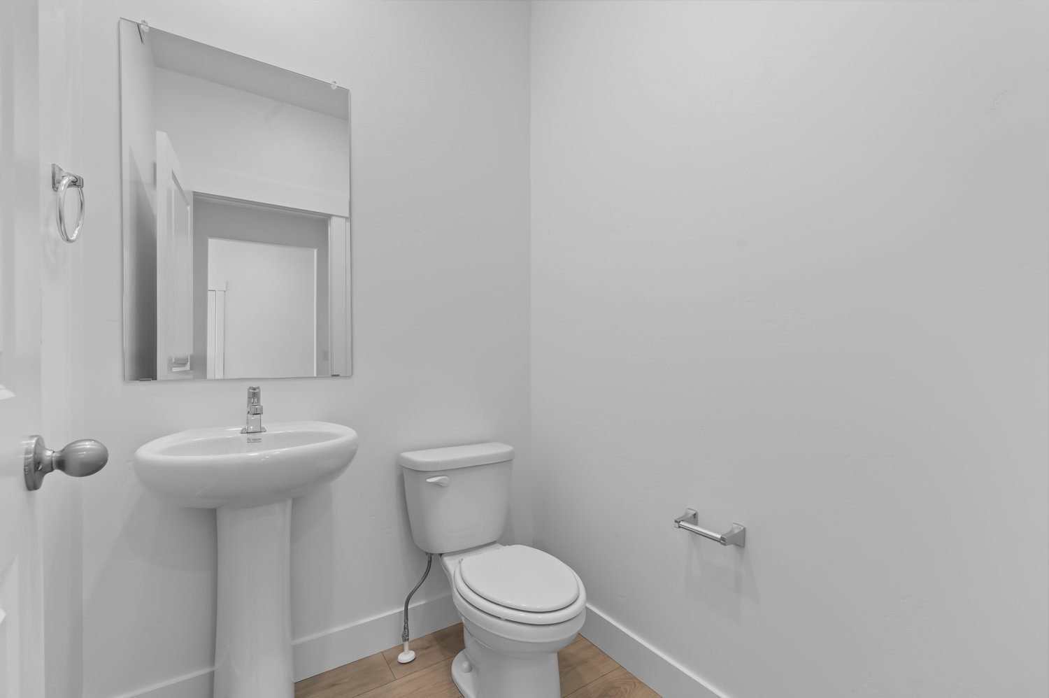 Pedestal sink with chrome faucet, wall-mounted mirror, white toilet, and wood-finish flooring