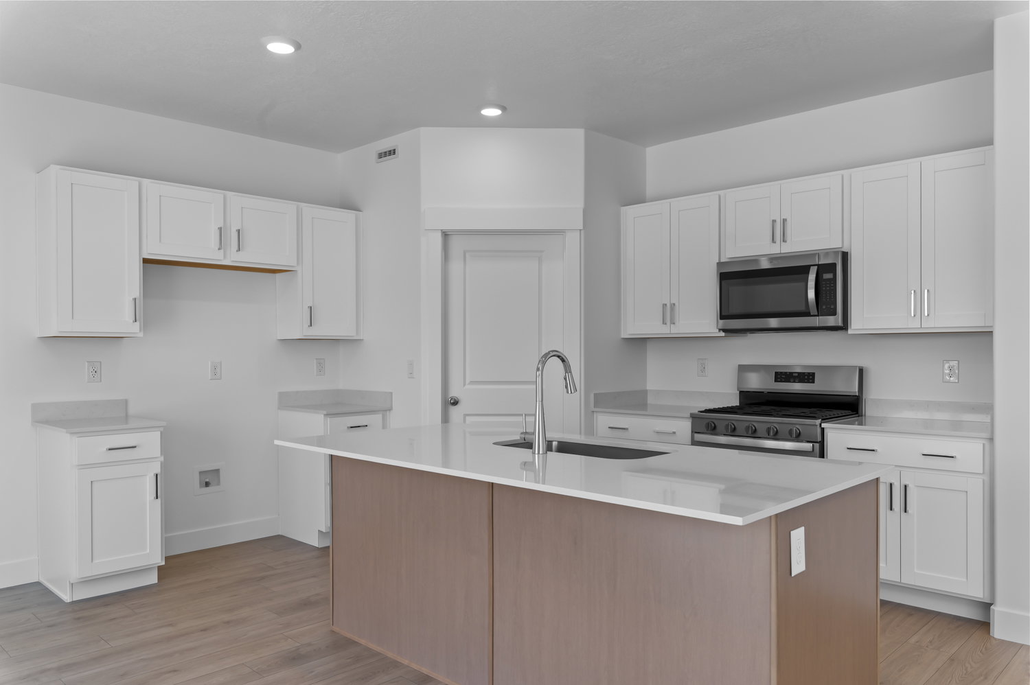 Kitchen featuring white shaker-style cabinetry, stainless steel appliances, a central island with wood-finish paneling, light-toned countertops, and wood-finish flooring