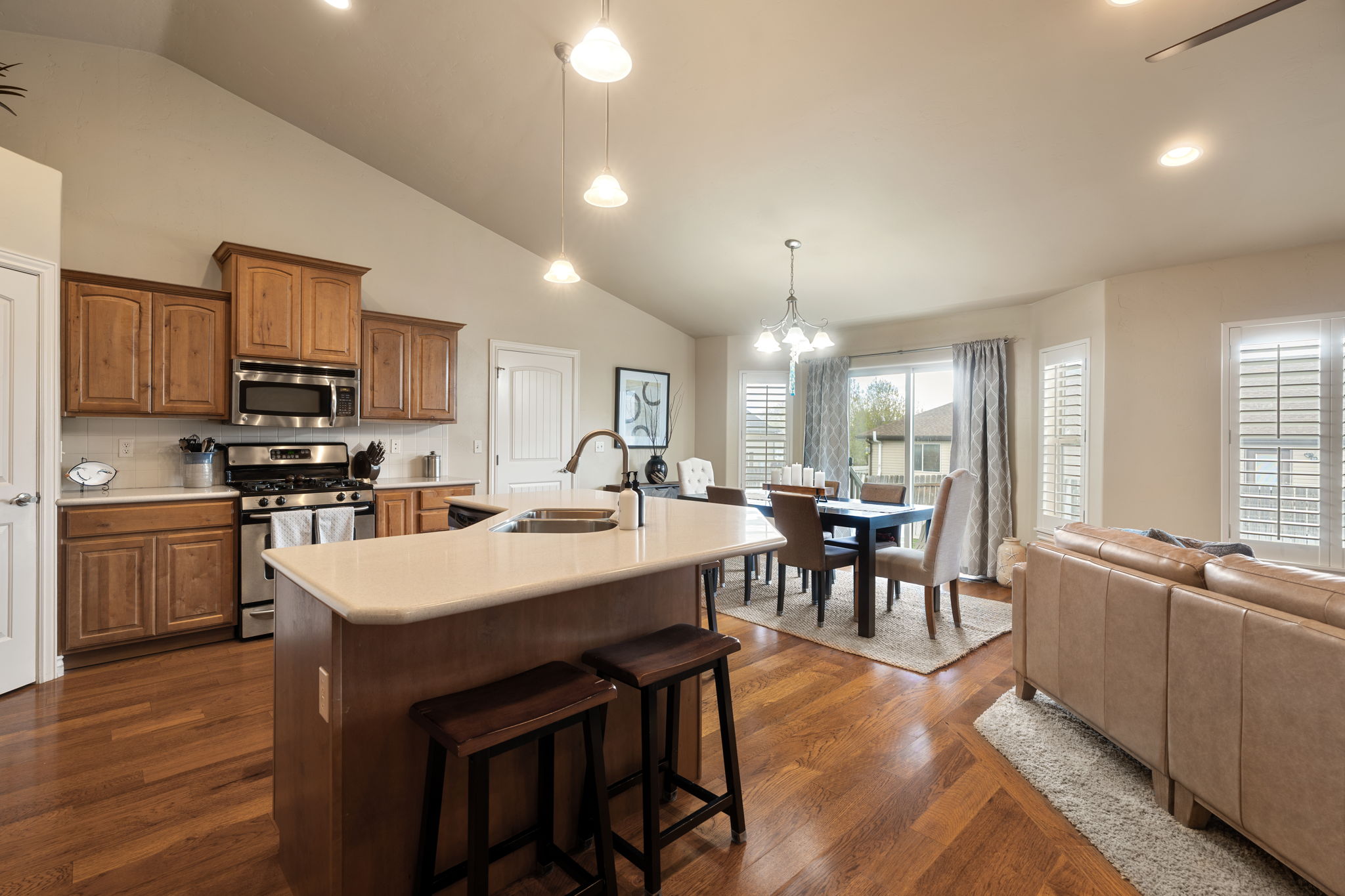 Kitchen with stainless steel appliances, light countertops, lofted ceiling, a kitchen island with sink, and wood finish cabinetry