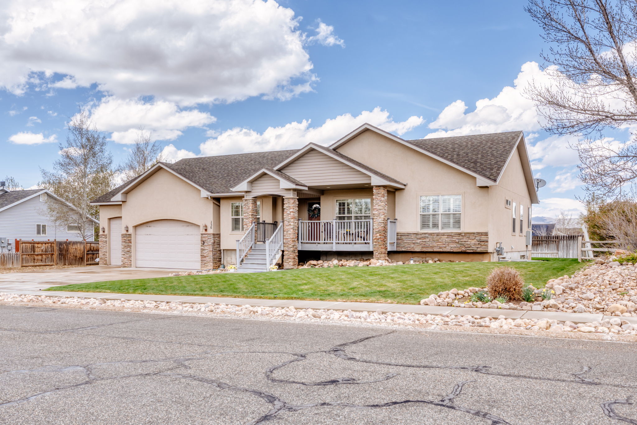 View of front of house with stone siding, stucco siding, a shingled roof, a porch, and a garage