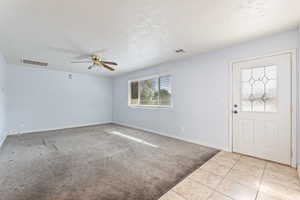 Foyer entrance with a ceiling fan, light carpet, light tile patterned floors, and a textured ceiling
