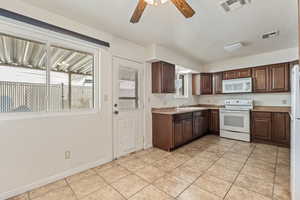 Kitchen with a ceiling fan, white appliances, light countertops, dark wood finish cabinetry, and light tile patterned floors