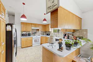 Kitchen with a peninsula, lofted ceiling, stainless steel appliances, tasteful backsplash, and light countertops