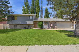 Split level home featuring a front yard, brick siding, a garage, and concrete driveway