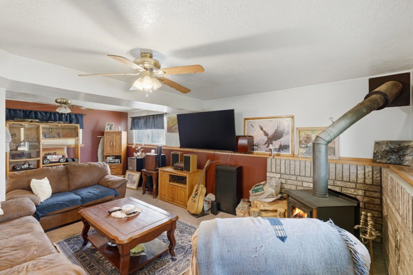 Carpeted living room with a wood stove, a textured ceiling, and ceiling fan