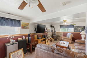 Living area featuring a wood stove, a textured ceiling, ceiling fan, and light carpet