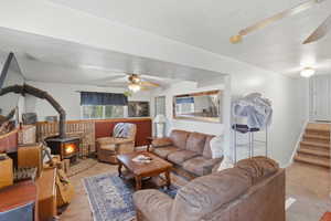 Living area with ceiling fan, a wood stove, light colored carpet, and a textured ceiling