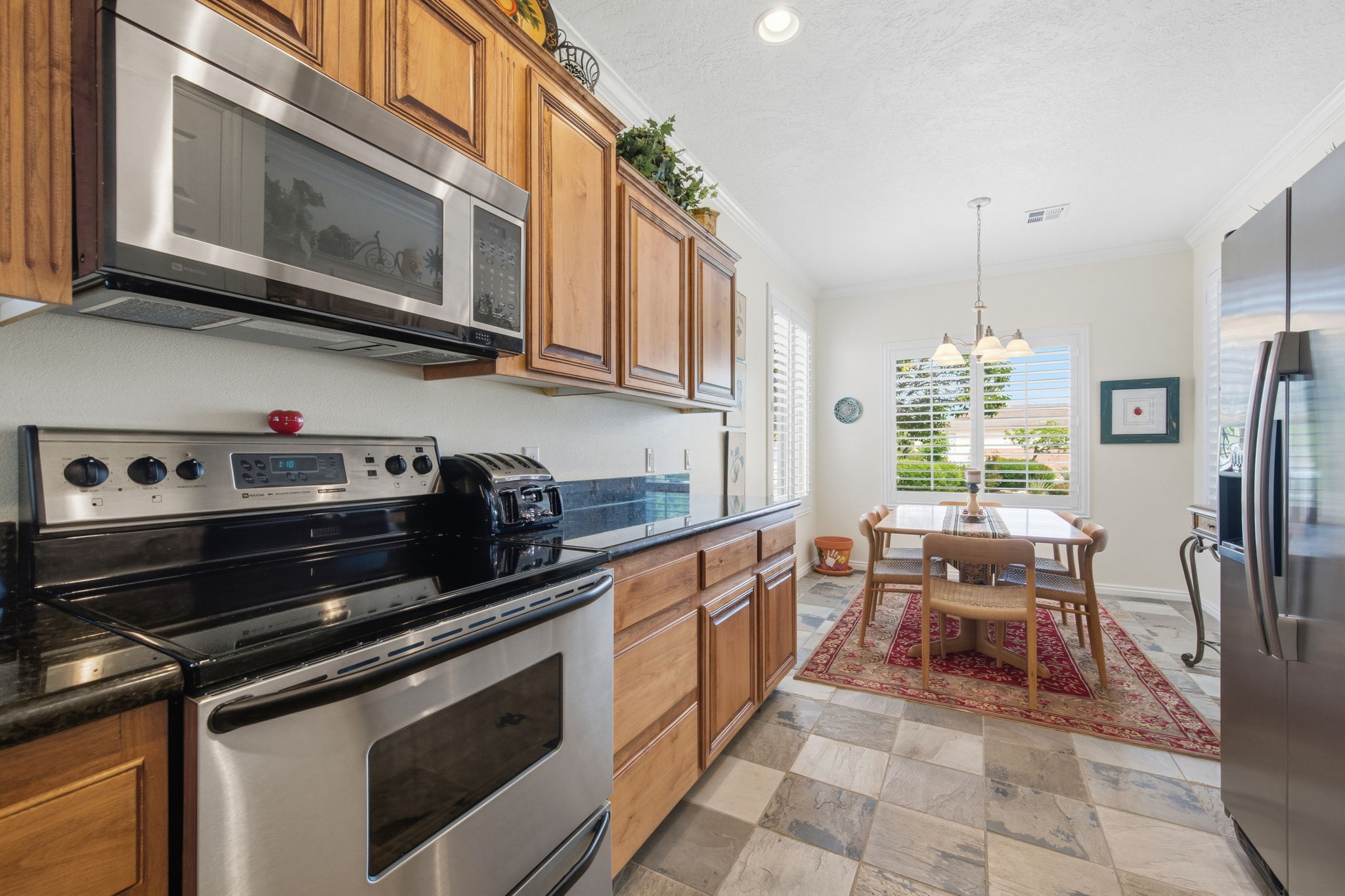 Kitchen featuring stainless steel appliances, wood finish cabinetry, crown molding, dark stone countertops, and hanging lights