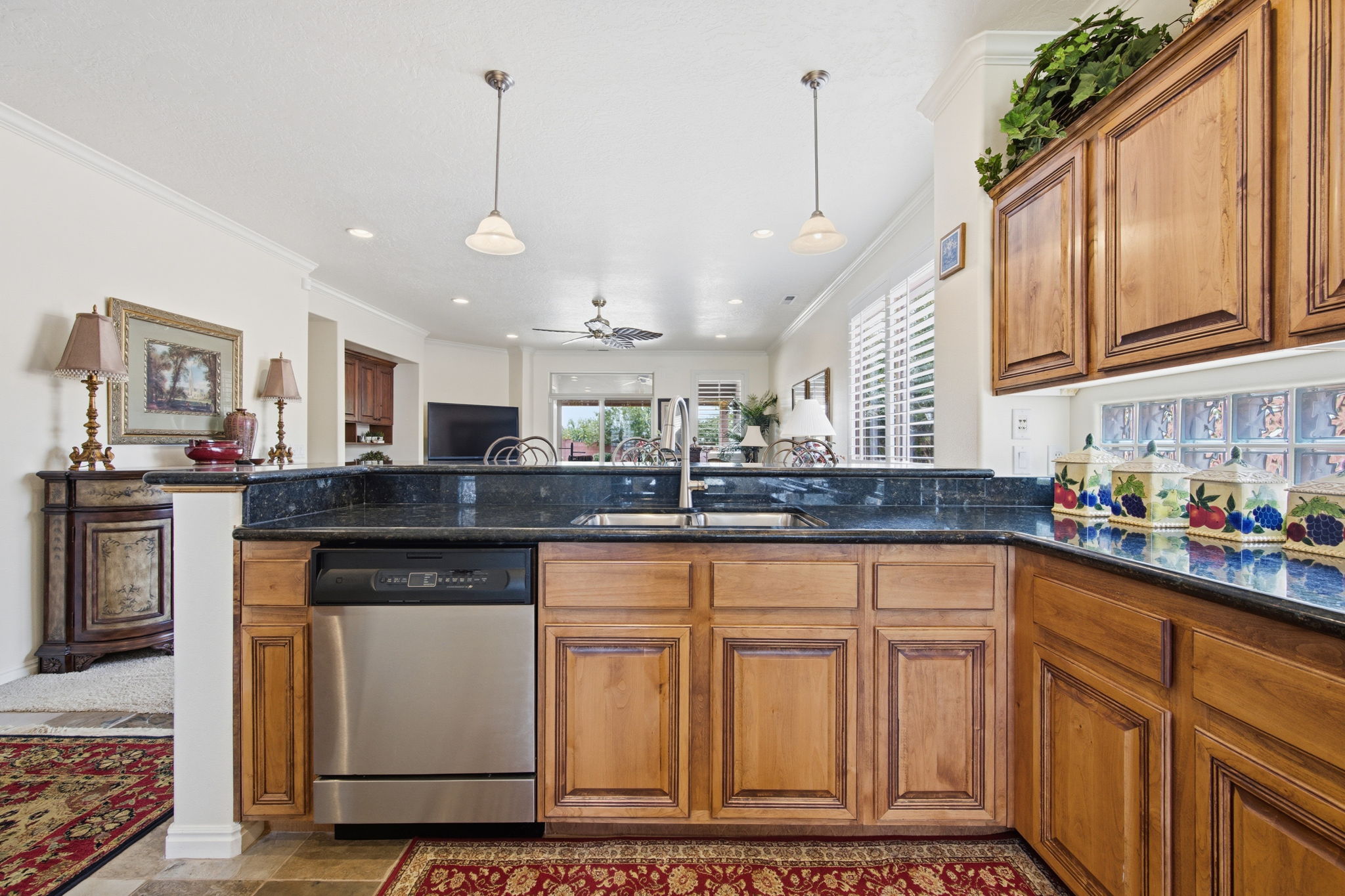 Kitchen with wood finish cabinetry, hanging light fixtures, stainless steel dishwasher, open floor plan, and dark stone countertops