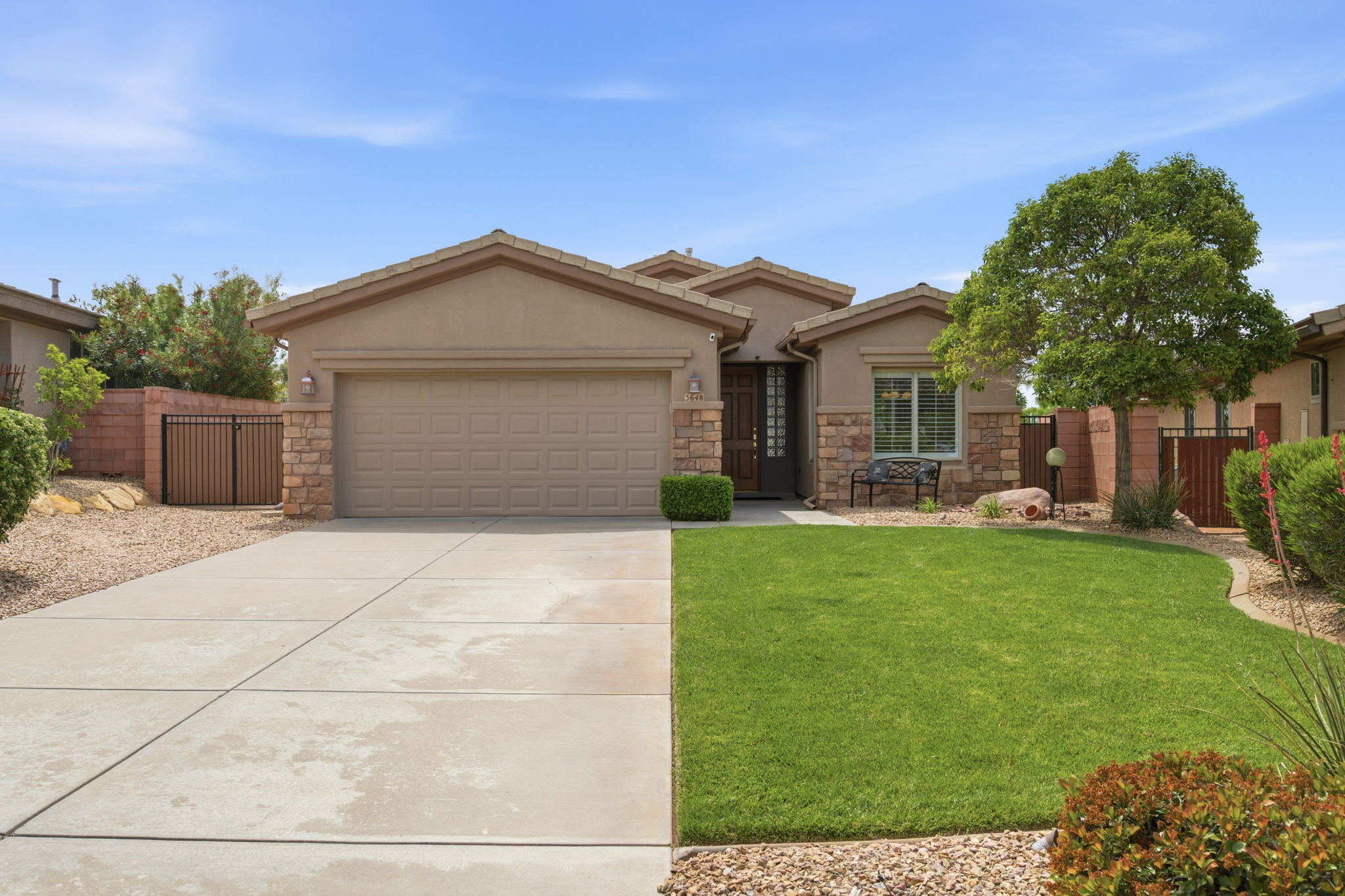 Single story home featuring stucco siding, a garage, driveway, a gate, and stone siding