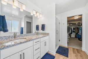 Full bath with a spacious closet, double vanity, a shower stall, light wood-style flooring, and a textured ceiling
