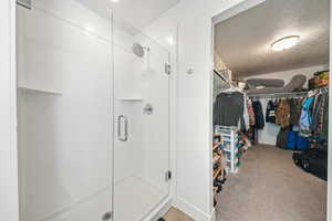Full bathroom featuring a spacious closet, a shower stall, a textured ceiling, and light carpet