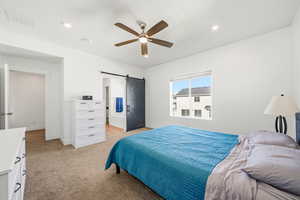 Bedroom featuring a ceiling fan, ensuite bath, light colored carpet, a barn door, and recessed lighting