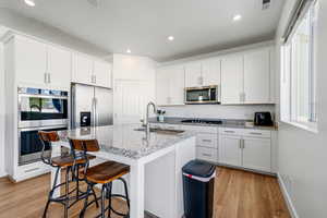 Kitchen featuring stainless steel appliances, white cabinetry, healthy amount of natural light, light stone counters, and recessed lighting