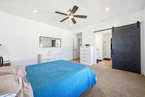 Bedroom featuring a barn door, a ceiling fan, light carpet, ensuite bathroom, and recessed lighting