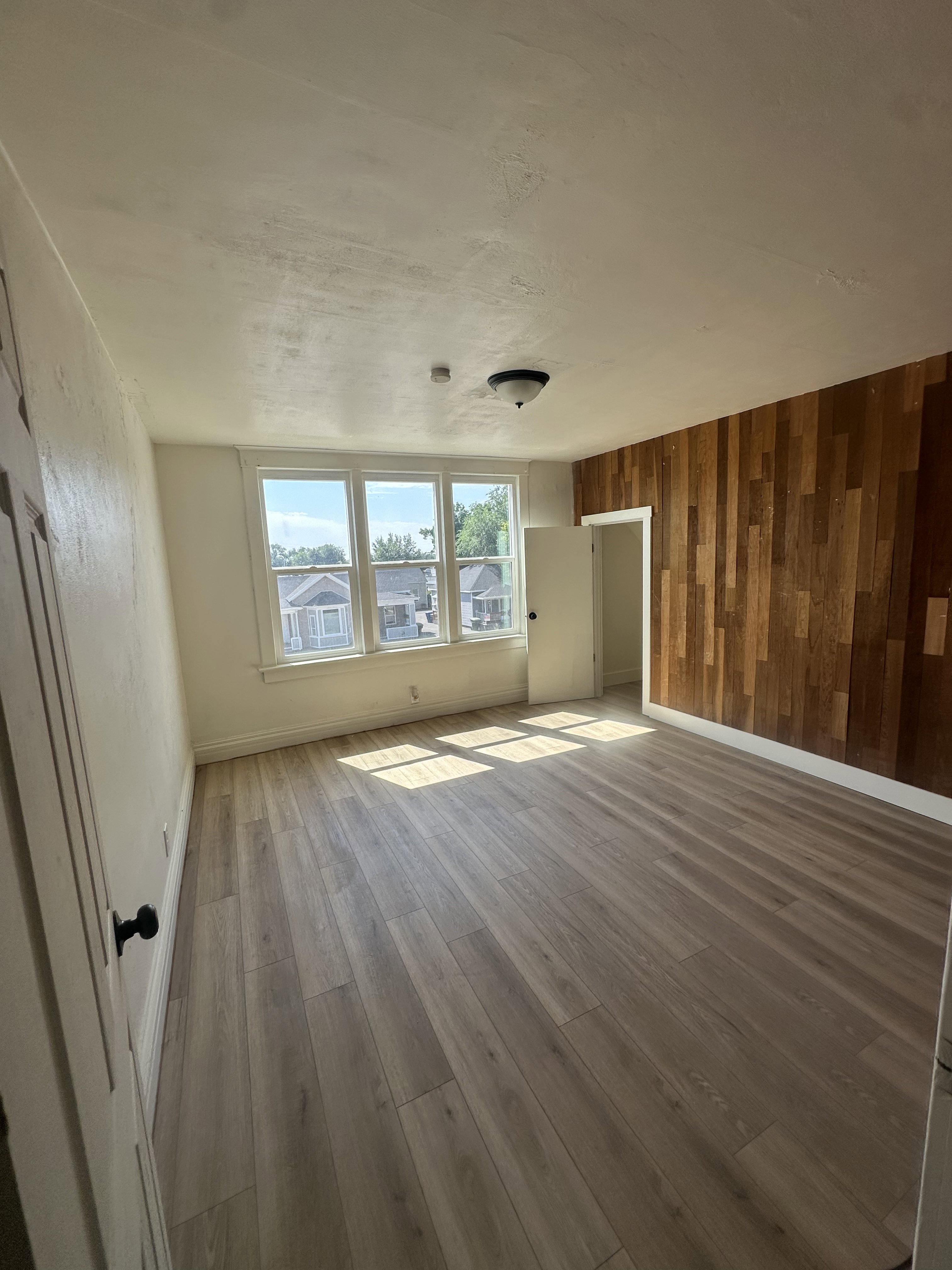 Room featuring light wood-finish flooring, a wood-paneled accent wall, and multiple windows