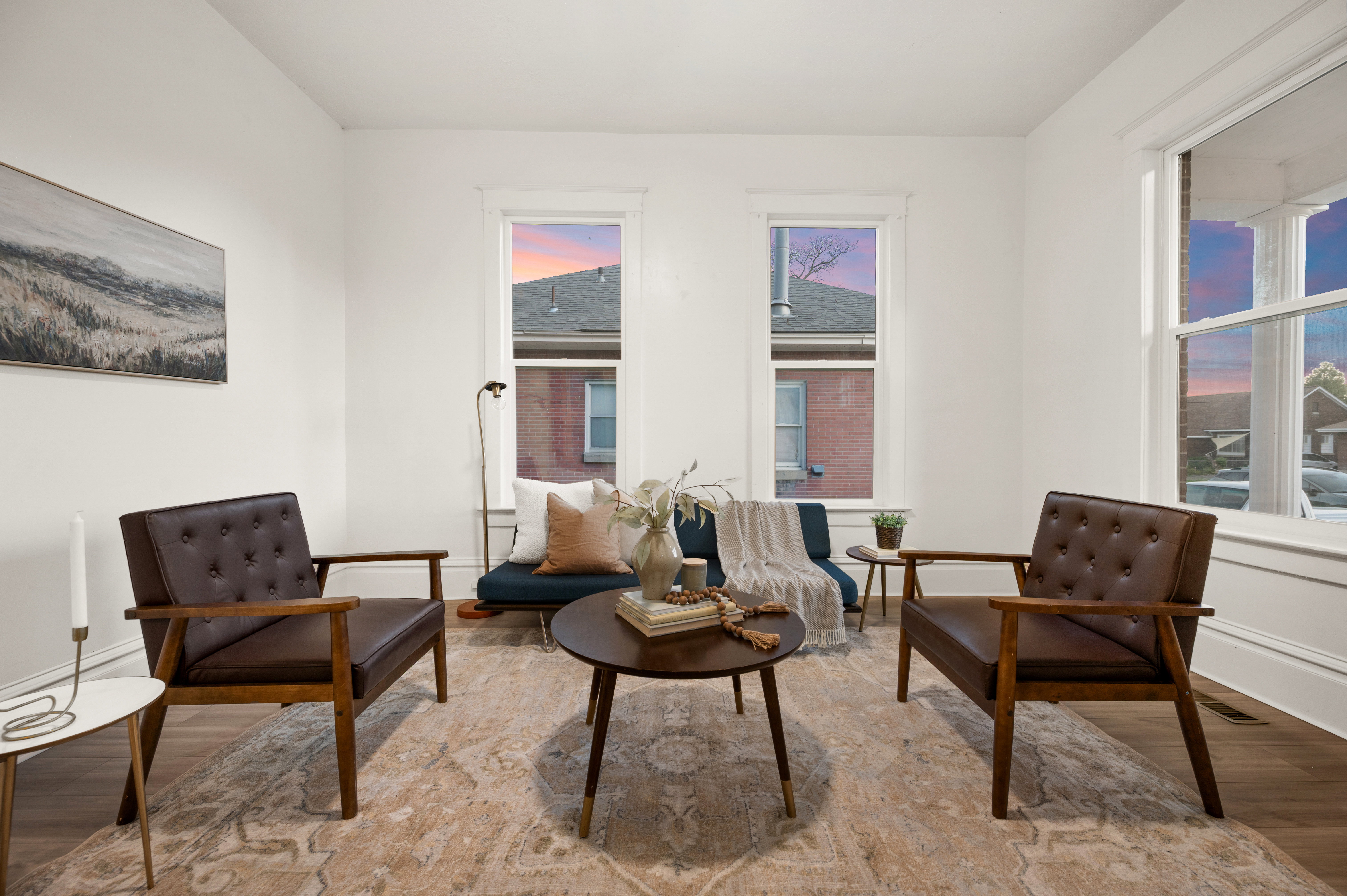Bright interior space featuring light-toned walls, multiple windows with white trim, wood-finish flooring, and a decorative area rug