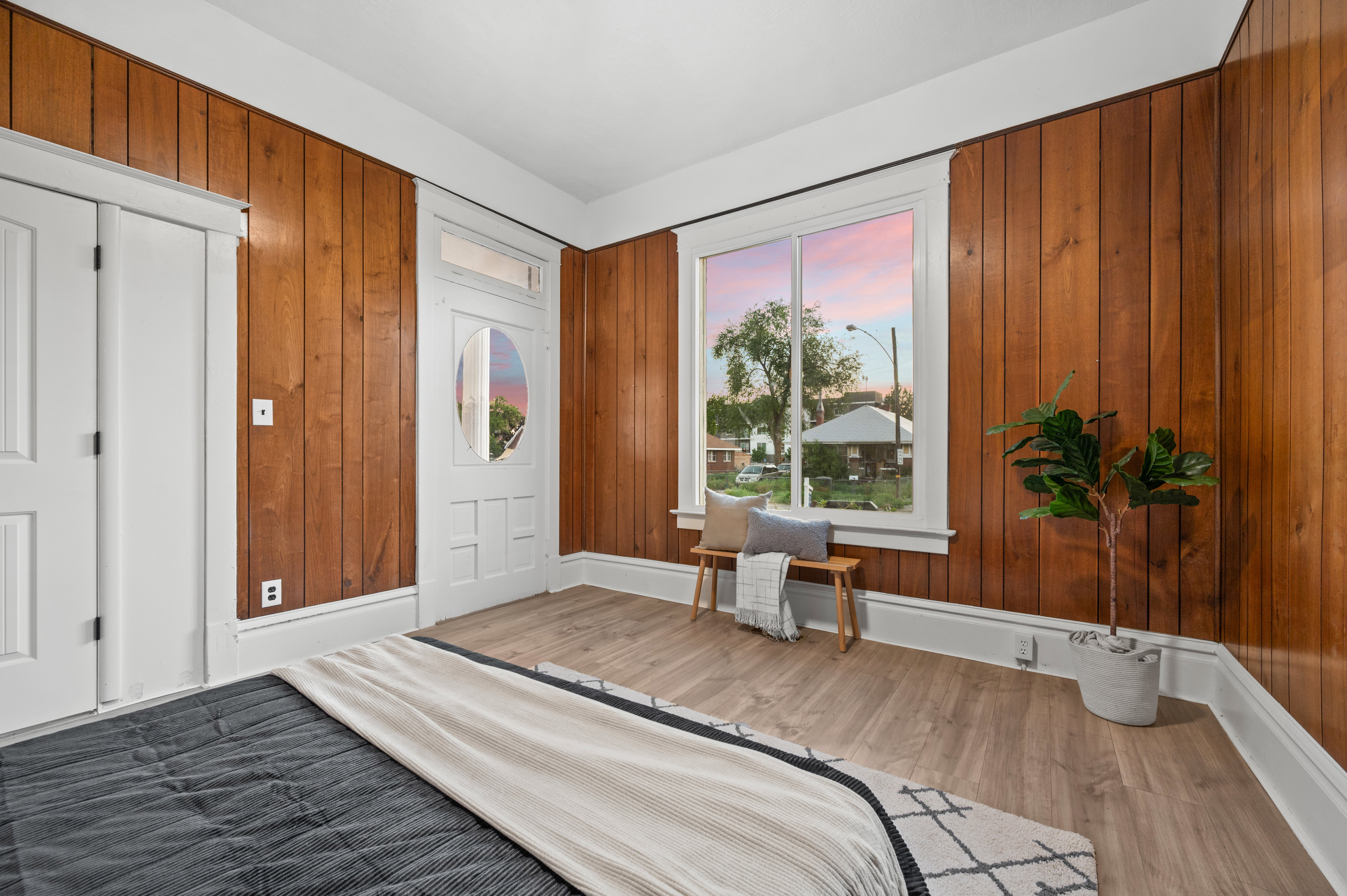 Room featuring warm wood paneling, white trim, wood-finish flooring, a prominent window, and a white interior door with an oval glass insert