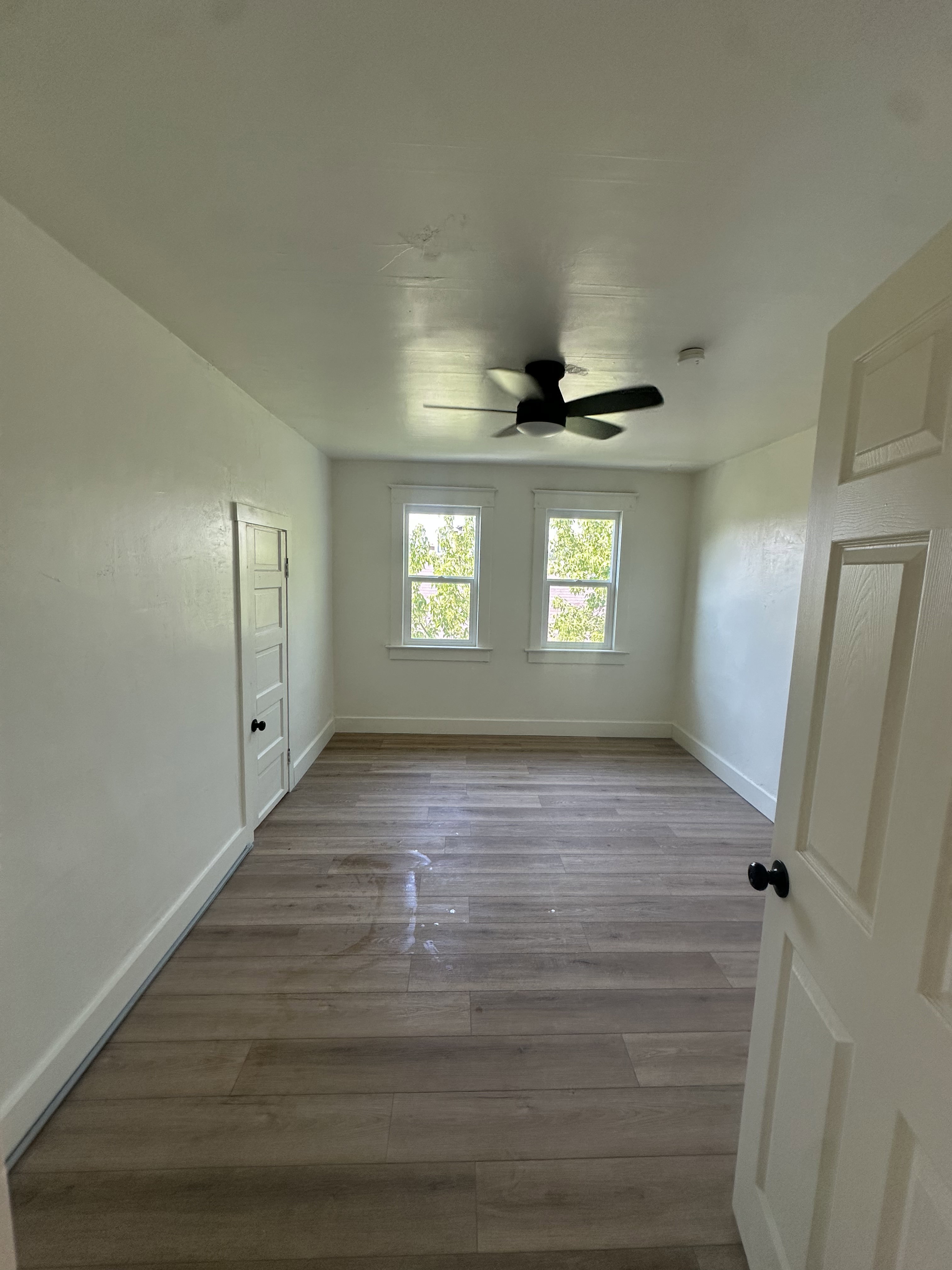 Spacious room featuring wood-finish flooring, white walls, and a ceiling fan