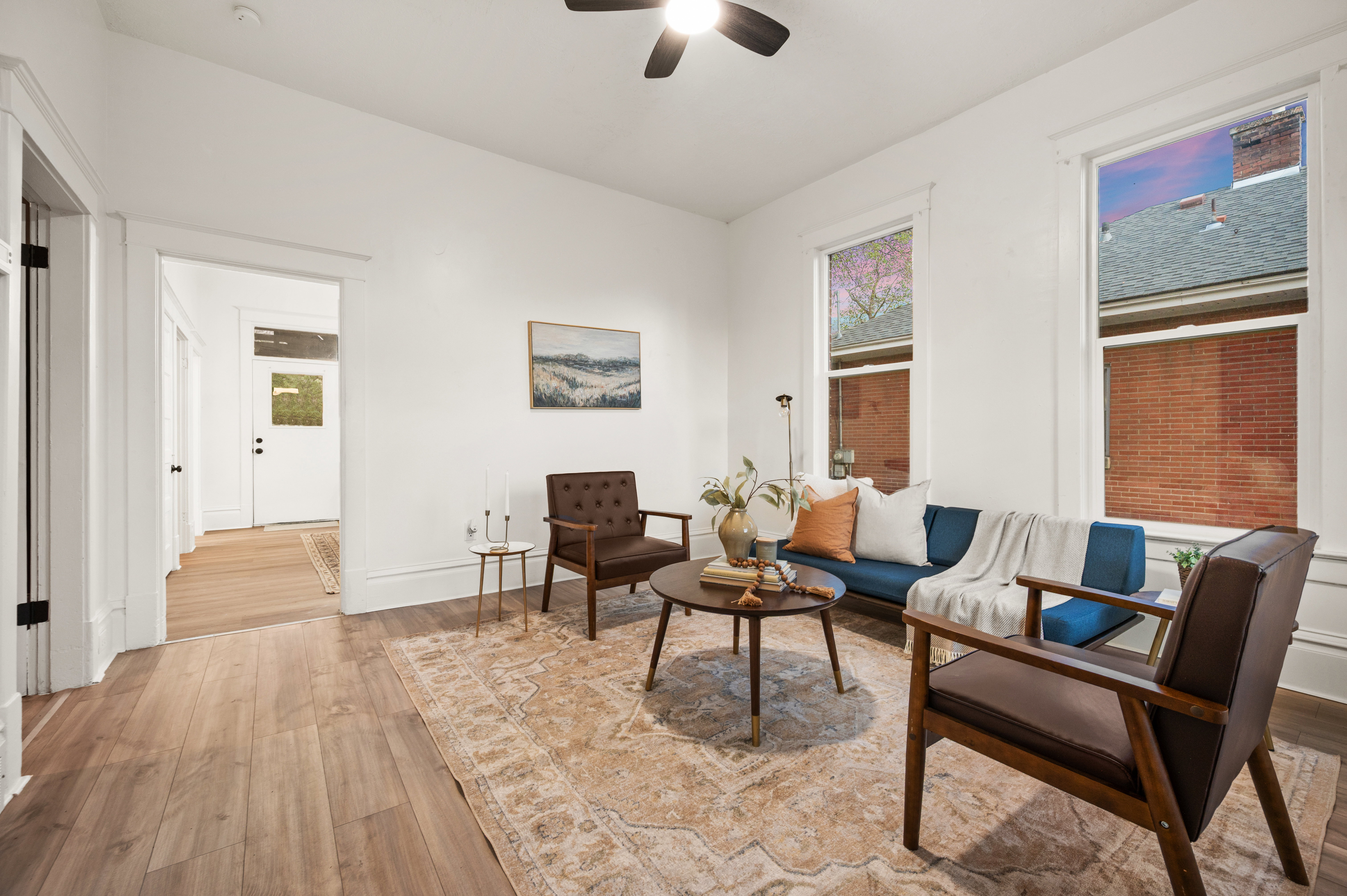 Bright living area with wood-finish flooring, white trim, and a ceiling fan