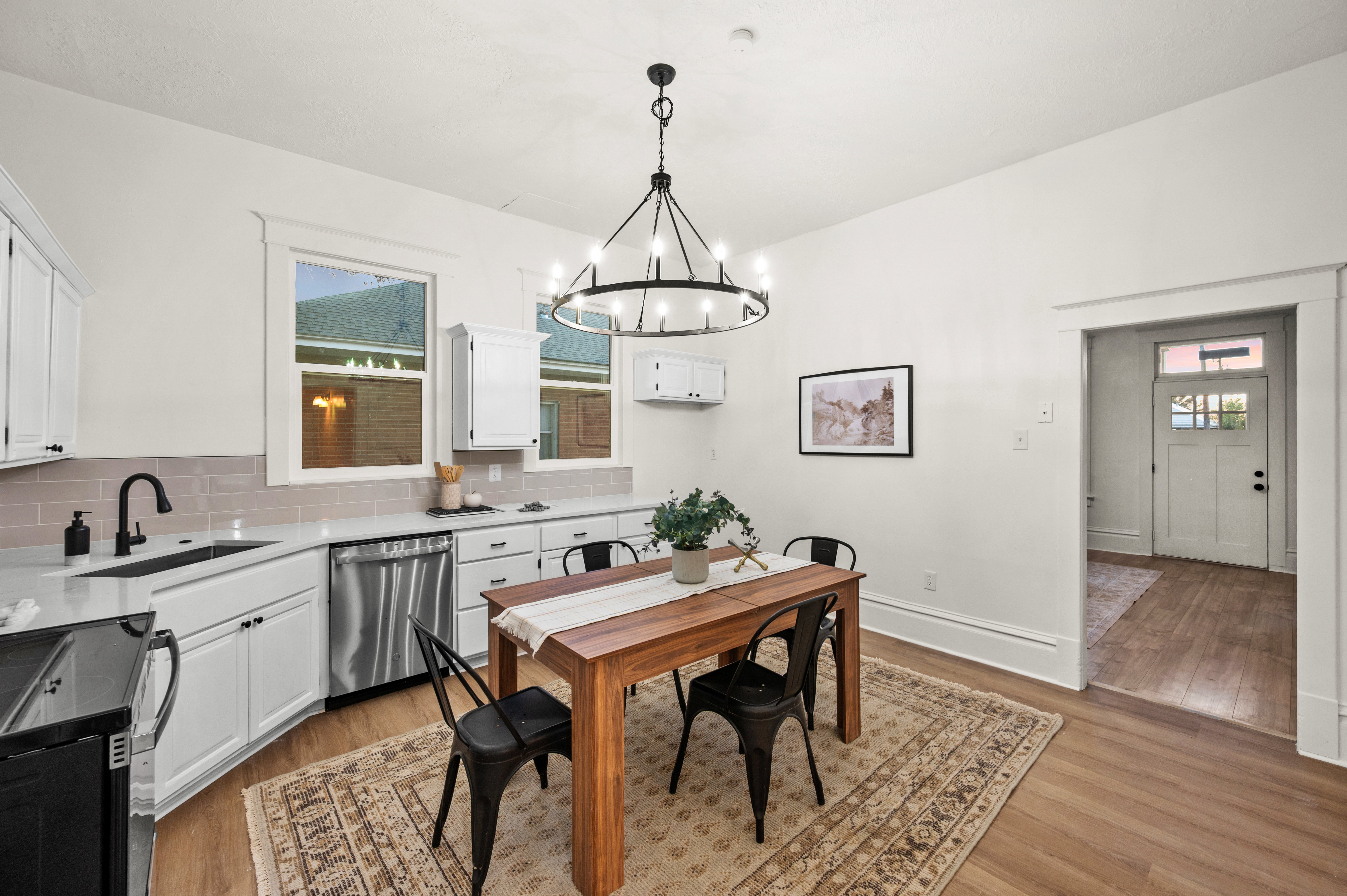 Integrated kitchen and dining area featuring white cabinetry, light countertops, stainless steel dishwasher, and wood-finish flooring
