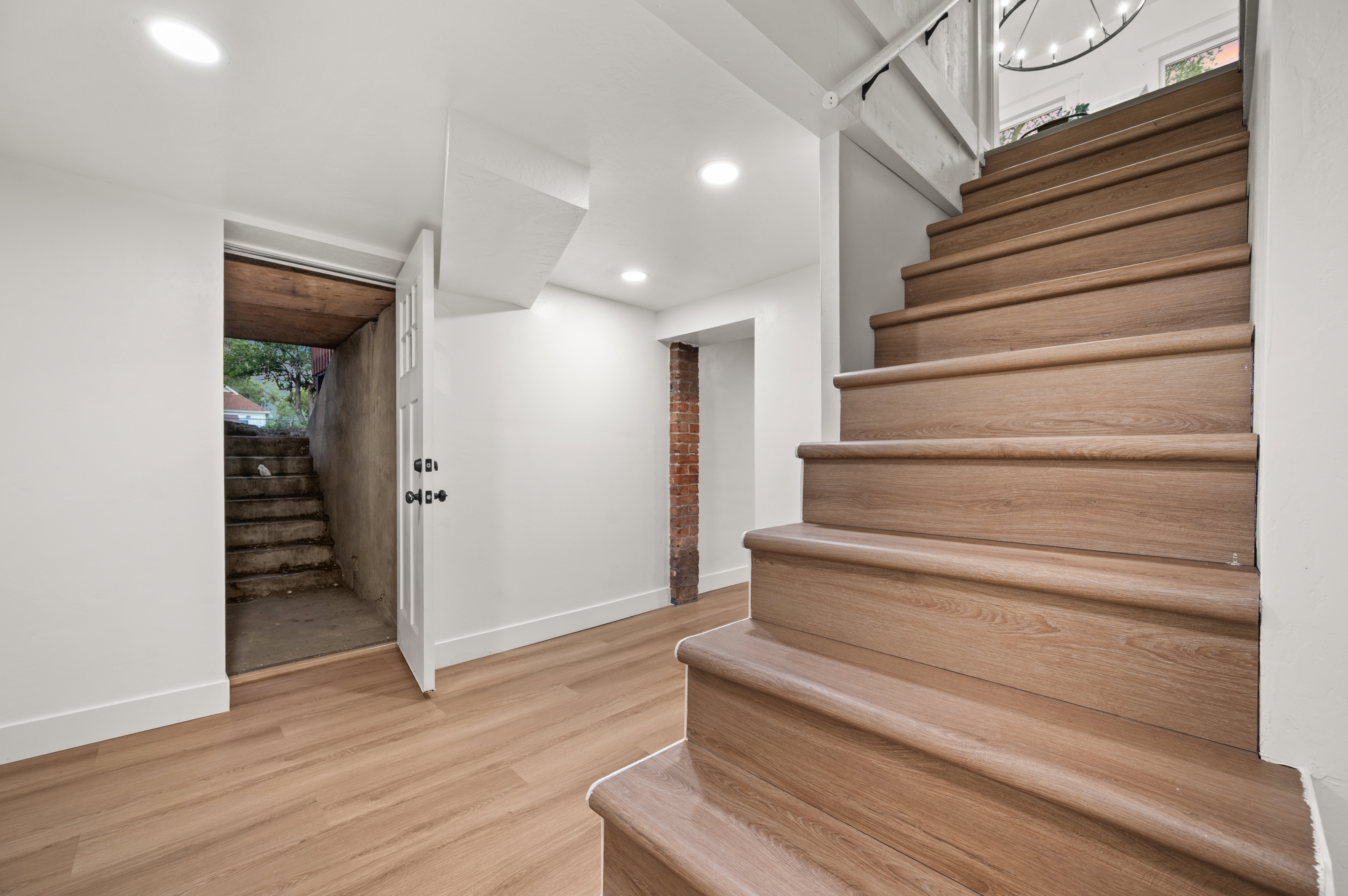 Wood-finish flooring and staircase with recessed lighting, white walls, and a visible brick accent wall