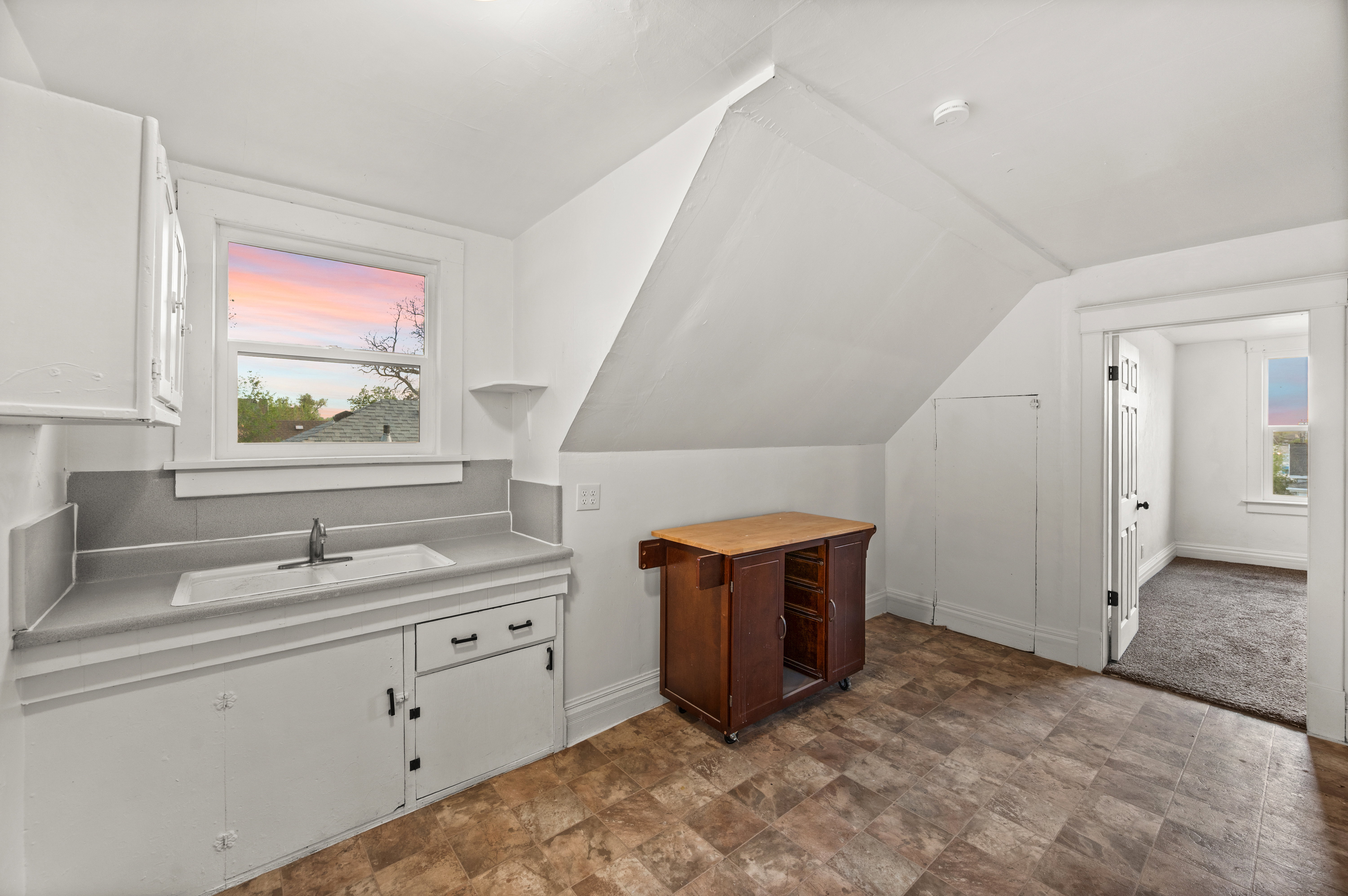 Kitchen with light countertops, white cabinets, stone finish floors, and lofted ceiling